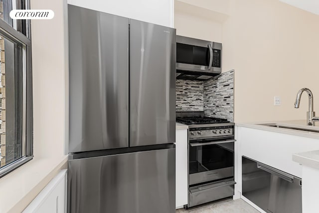 kitchen with stainless steel appliances, backsplash, white cabinetry, sink, and light tile floors