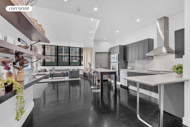 kitchen featuring backsplash, stainless steel appliances, sink, wall chimney range hood, and a kitchen breakfast bar