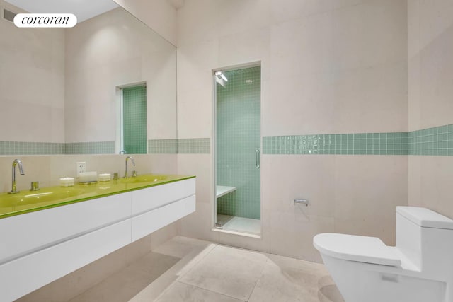 bathroom featuring tile walls, double sink vanity, a shower with door, and toilet