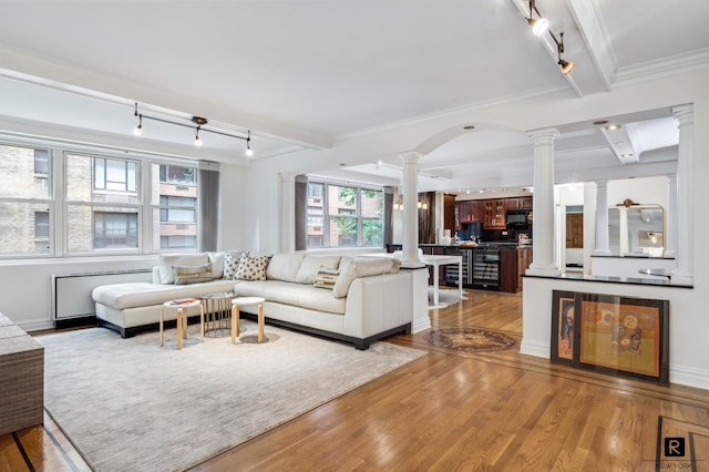 living room featuring beamed ceiling, track lighting, ornate columns, wood-type flooring, and ornamental molding