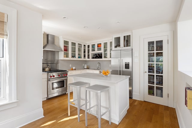 kitchen with white cabinets, a kitchen island, wall chimney range hood, and premium appliances