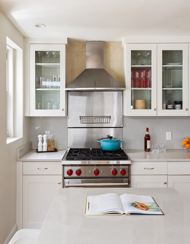 kitchen with white cabinets, high end range, and wall chimney range hood