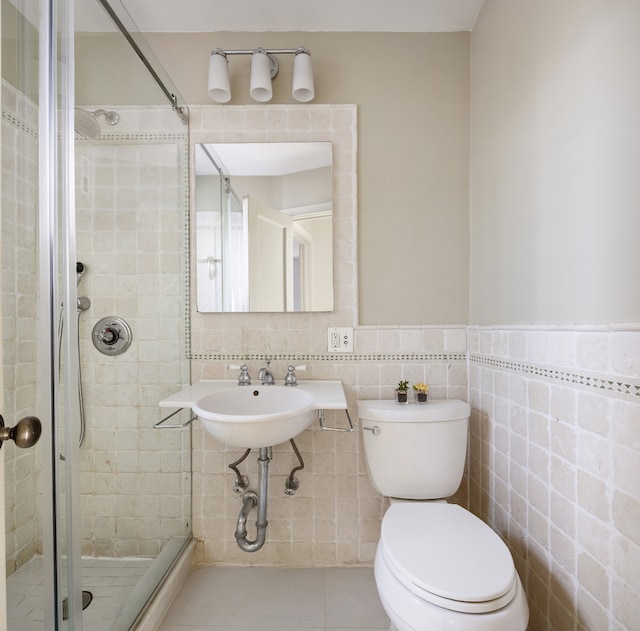 bathroom with tile patterned floors, toilet, a shower with shower door, and tile walls