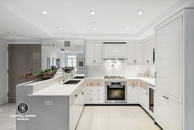 kitchen featuring kitchen peninsula, white cabinets, beverage cooler, stainless steel appliances, and sink