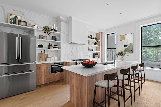 kitchen featuring crown molding, an island with sink, light wood-type flooring, sink, and appliances with stainless steel finishes