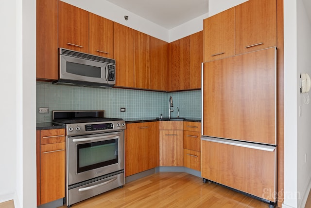 kitchen featuring decorative backsplash, sink, dark stone countertops, appliances with stainless steel finishes, and light hardwood / wood-style flooring