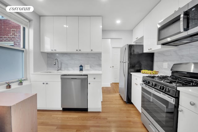 kitchen featuring white cabinetry, tasteful backsplash, stainless steel appliances, sink, and light hardwood / wood-style flooring