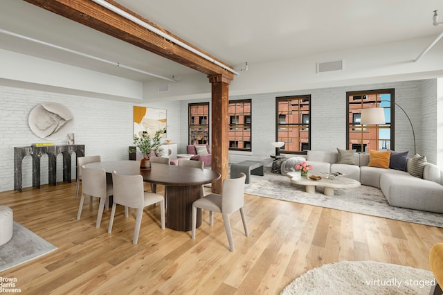 dining room with ornate columns, a fireplace, brick wall, and light wood-type flooring