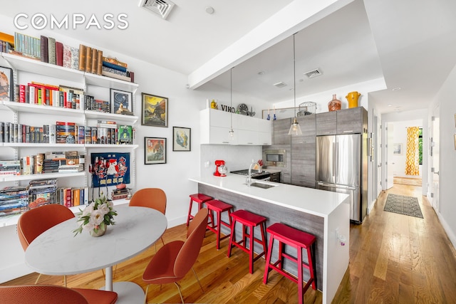 kitchen with appliances with stainless steel finishes, sink, light wood-type flooring, kitchen peninsula, and a breakfast bar area