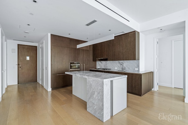 kitchen featuring tasteful backsplash, sink, dark brown cabinetry, light wood-type flooring, and a center island