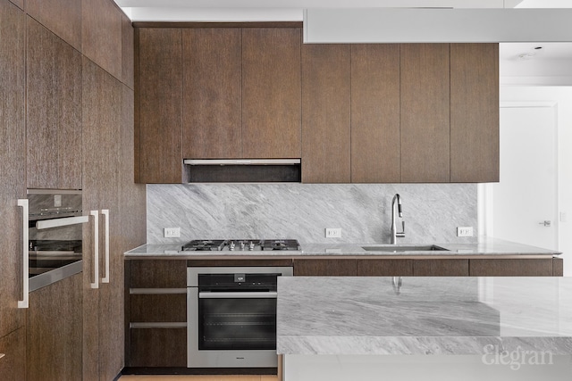 kitchen featuring sink, range hood, light stone counters, appliances with stainless steel finishes, and backsplash