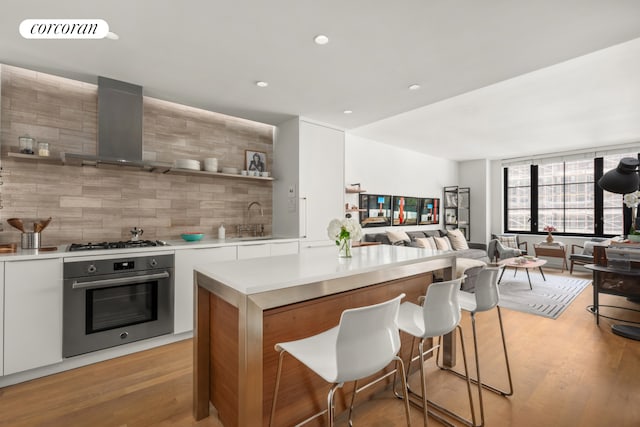 kitchen featuring stainless steel appliances, decorative backsplash, wall chimney exhaust hood, sink, and light hardwood / wood-style flooring