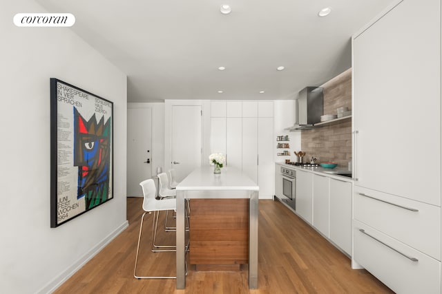 kitchen featuring white cabinetry, tasteful backsplash, light wood-type flooring, wall chimney exhaust hood, and oven