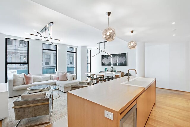 kitchen with pendant lighting, sink, stainless steel microwave, light hardwood / wood-style flooring, and a kitchen island with sink