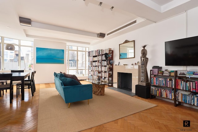 living room with a raised ceiling, light parquet flooring, a wall of windows, and a premium fireplace