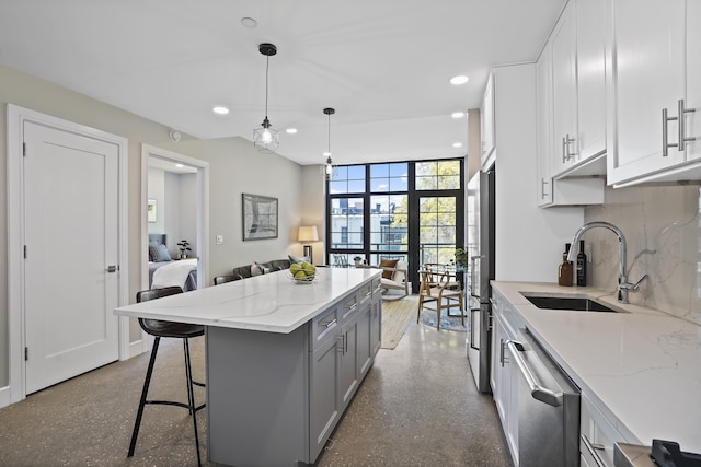 kitchen with a kitchen bar, stainless steel appliances, sink, decorative light fixtures, and white cabinets