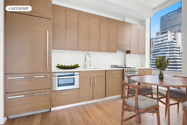 kitchen with wall oven, light wood-type flooring, ventilation hood, sink, and high end stove