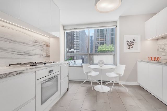 kitchen featuring white oven, white cabinets, light tile patterned floors, and stainless steel gas cooktop