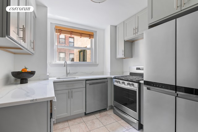 kitchen with stainless steel appliances, gray cabinetry, sink, light stone counters, and light tile patterned flooring