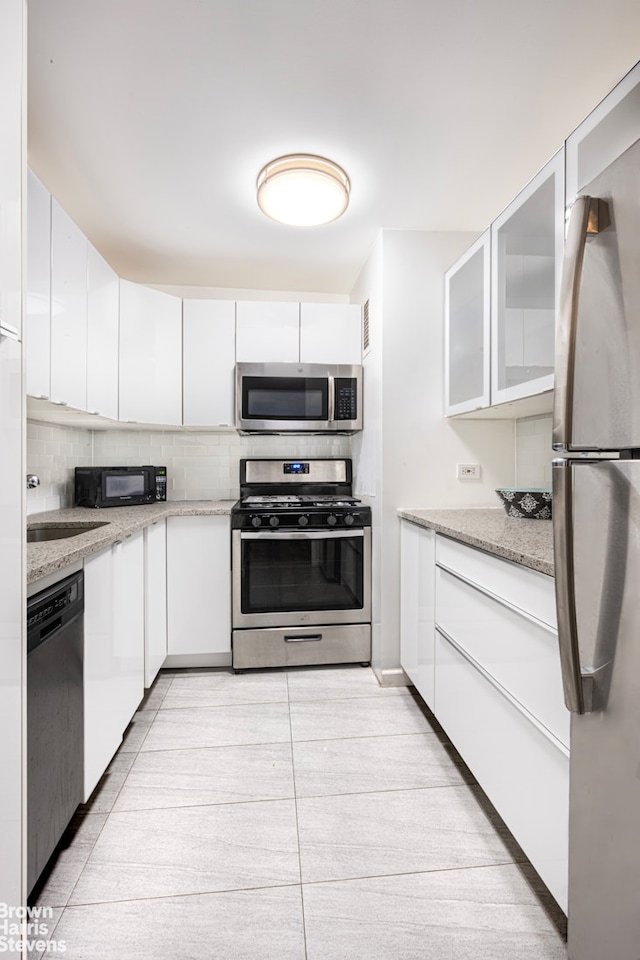 kitchen with appliances with stainless steel finishes, decorative backsplash, white cabinets, and light tile patterned floors