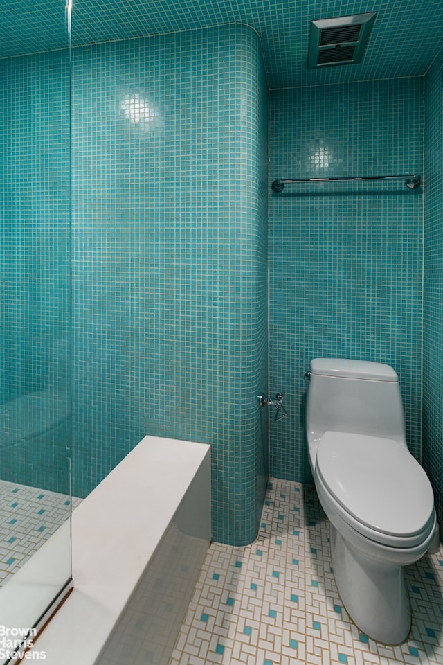 bathroom featuring a tile shower, toilet, and tile walls