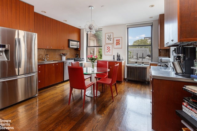 kitchen featuring appliances with stainless steel finishes, sink, decorative light fixtures, radiator heating unit, and dark hardwood / wood-style floors