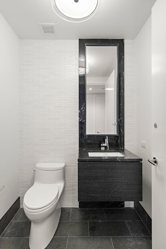 bathroom with toilet, vanity, and tile walls