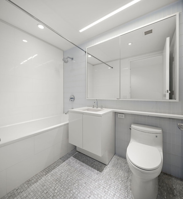 full bathroom featuring tile walls, toilet, vanity, tiled shower / bath combo, and tile patterned floors