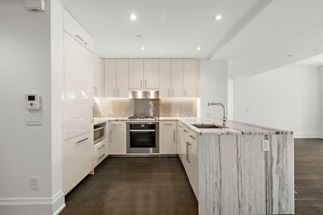 kitchen featuring sink, kitchen peninsula, white cabinetry, stainless steel appliances, and dark wood-type flooring