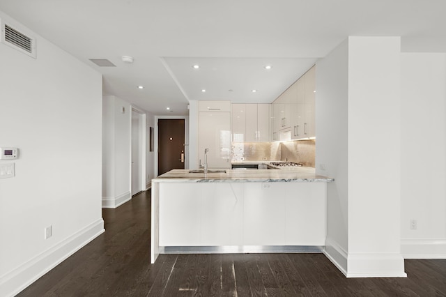 kitchen featuring tasteful backsplash, sink, dark hardwood / wood-style flooring, kitchen peninsula, and white cabinets