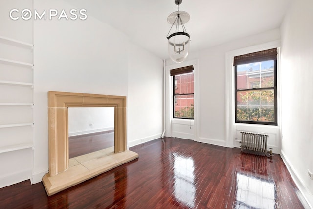 unfurnished living room featuring built in features, dark wood-type flooring, and radiator heating unit