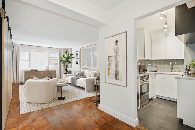 interior space featuring stainless steel stove, a barn door, white cabinetry, sink, and dark parquet floors