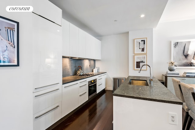 kitchen with white cabinets, sink, backsplash, appliances with stainless steel finishes, and dark hardwood / wood-style floors