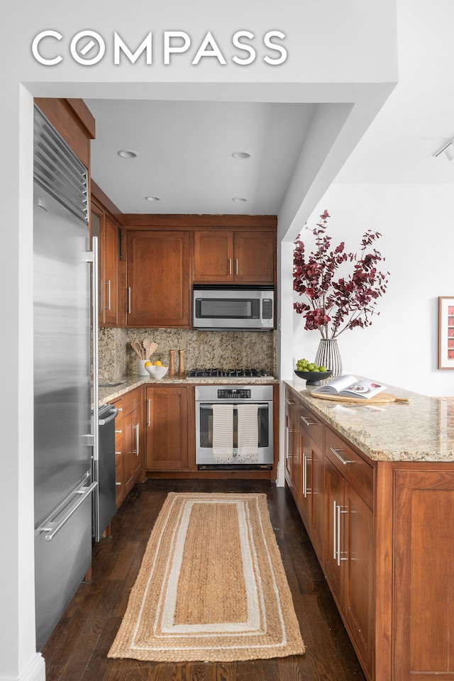 kitchen featuring appliances with stainless steel finishes, dark hardwood / wood-style flooring, light stone counters, and backsplash