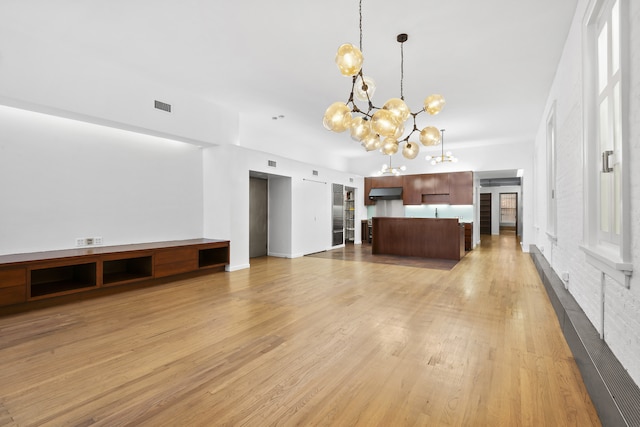 unfurnished living room with light wood-type flooring and a notable chandelier