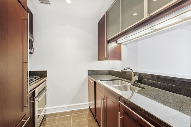 kitchen featuring dark stone counters, dark brown cabinets, appliances with stainless steel finishes, and sink