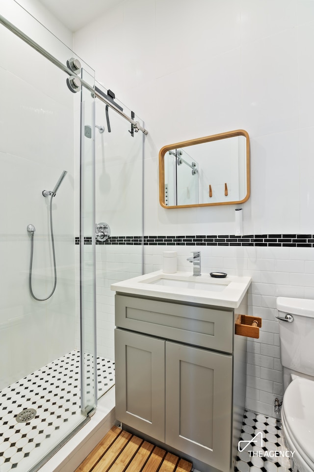 bathroom featuring a shower with door, vanity, hardwood / wood-style floors, tile walls, and toilet