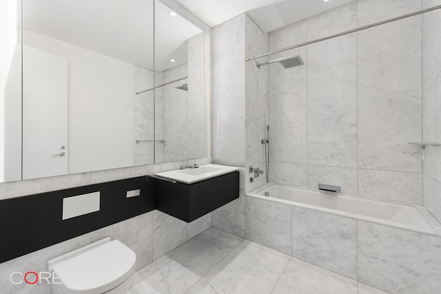 full bathroom featuring tile walls, vanity, tiled shower / bath, and toilet