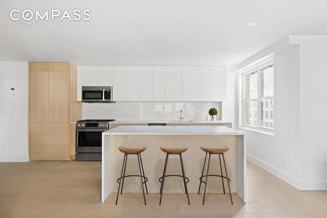 kitchen featuring a kitchen breakfast bar, light hardwood / wood-style floors, stainless steel appliances, and white cabinets