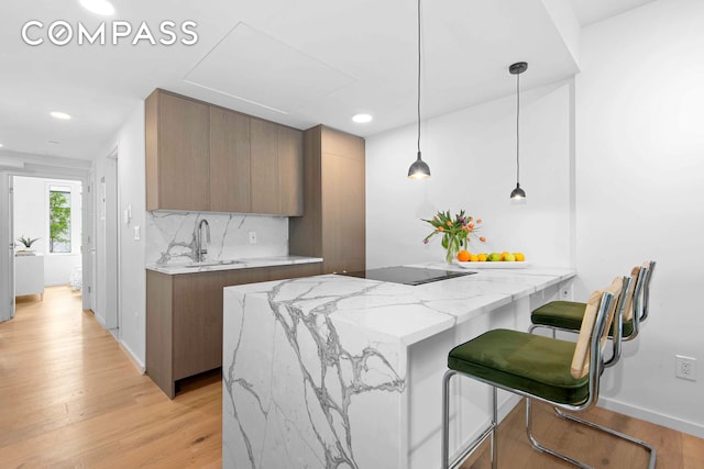 kitchen with light wood-type flooring, pendant lighting, a kitchen breakfast bar, light stone counters, and sink