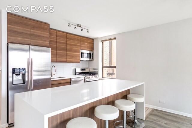 kitchen with sink, backsplash, light hardwood / wood-style floors, a breakfast bar, and appliances with stainless steel finishes