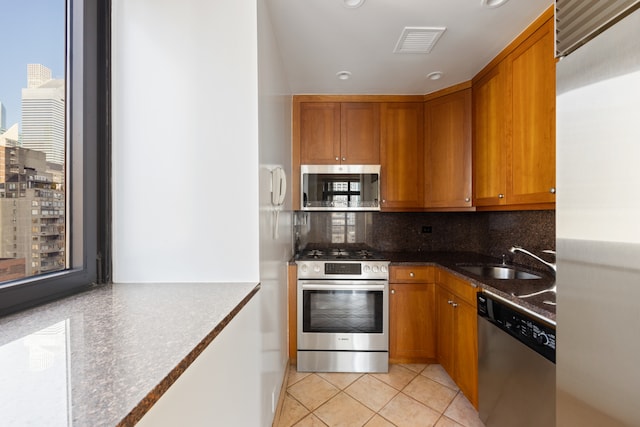 kitchen with sink, backsplash, stainless steel appliances, dark stone countertops, and light tile patterned floors