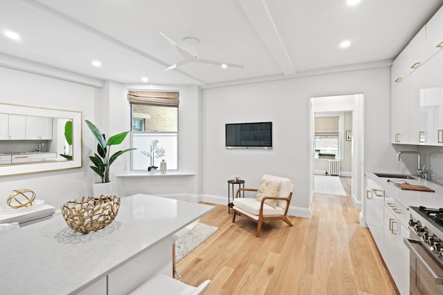 living area featuring light hardwood / wood-style floors, sink, beamed ceiling, and radiator heating unit