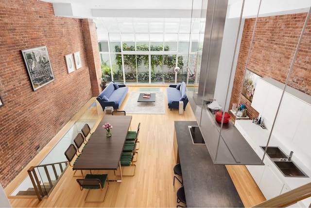 unfurnished living room with a high ceiling, light hardwood / wood-style floors, a wall of windows, and brick wall