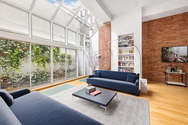 living room featuring wood-type flooring, brick wall, a high ceiling, and built in shelves