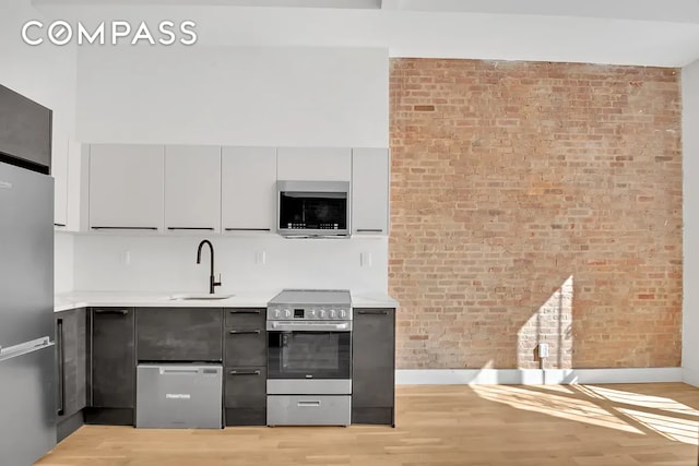 kitchen featuring sink, brick wall, light hardwood / wood-style flooring, gray cabinets, and stainless steel appliances