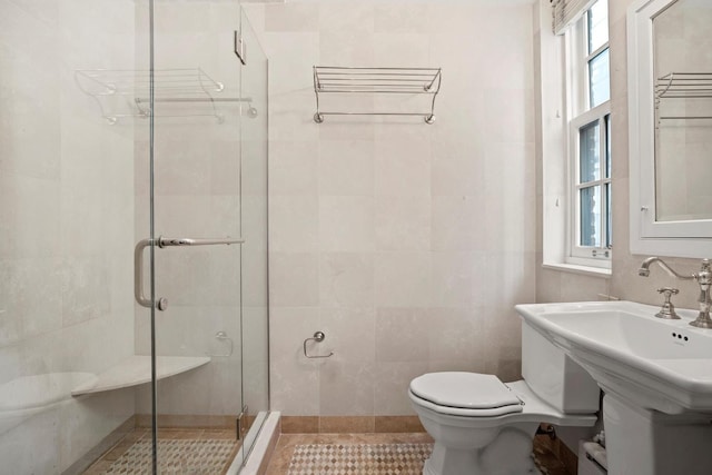 bathroom with tile walls, a shower with shower door, toilet, and tile patterned flooring