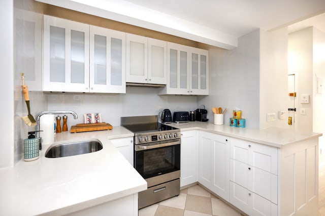 kitchen featuring decorative backsplash, kitchen peninsula, stainless steel range, sink, and white cabinets