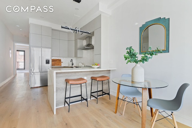 kitchen with wall chimney exhaust hood, light wood-type flooring, gray cabinetry, and built in refrigerator