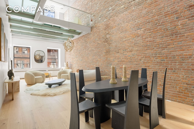 dining space featuring brick wall, light hardwood / wood-style flooring, and a high ceiling